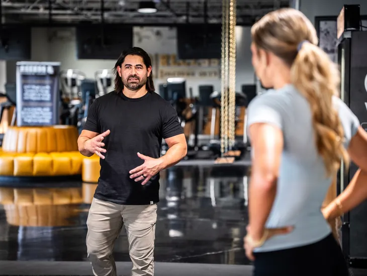 Coach Santiago walking a client through her training plan on the gym floor.